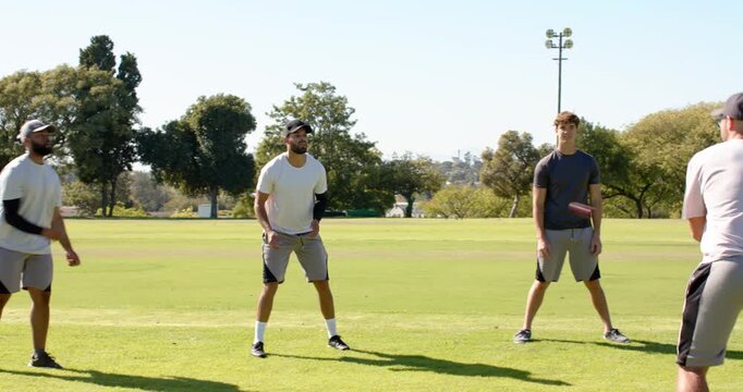 Diverse male friends doing warmup drills on park field, with baseball caps, compression sleeves