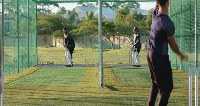 Diverse cricket teammates starting drill, pause, bowling, batting, retrieving balls in nets