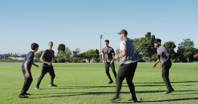 Diverse male teammates underhand tossing red ball on grass wearing sportswear practicing rotating