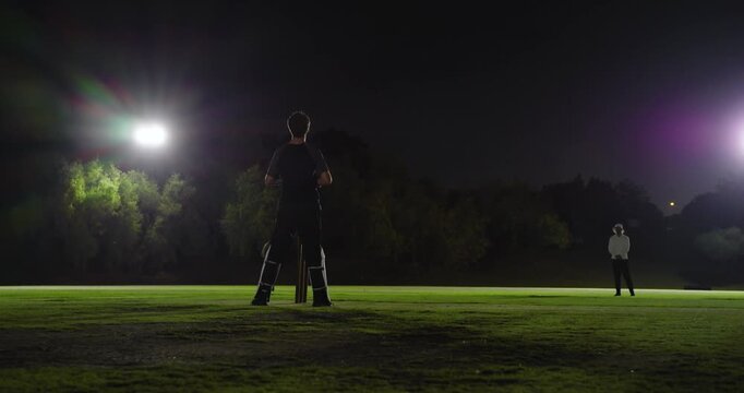 Bowler bowling, floodlights, batsman swinging, missing, keeper collecting, duo swapping ends