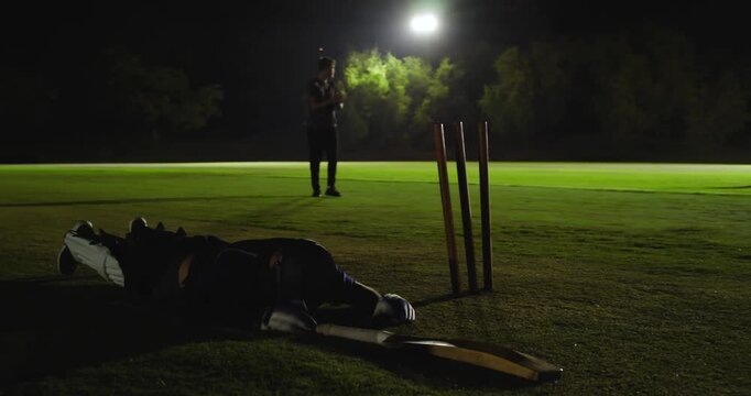 Diverse cricket team delivering ball lit pitch keeper diving dislodging bails dismissing batsman in