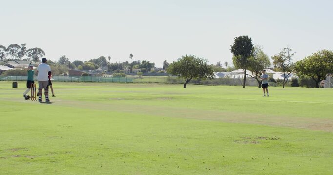 Asian bowler bowling ball in park, teen fielder catching ball, diverse male players celebrating