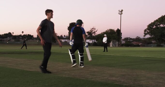 Teenage bowler bowling ball on pitch, batsman calling single, batting partners switching ends
