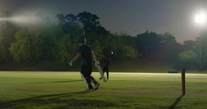 Diverse cricket partners hitting ball and calling run, sprinting between wickets on floodlit pitch