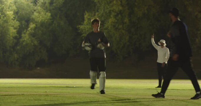 Batsman under floodlights hesitating after wicketkeeper underarming ball to stumps walking off