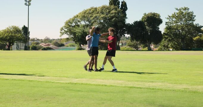 Friends hugging and approaching on grassy sports field, with shin guards and blue baseball cap
