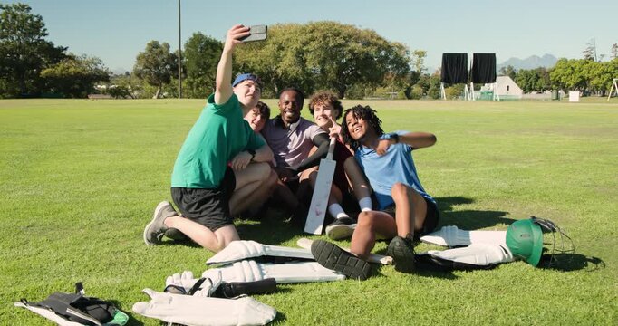 Five cricket teammates snapping selfie with smartphone on cricket field, showing bat and pads