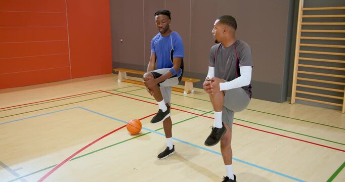 Dribbling african american male friends wearing sportswear on gym court, with basketballs