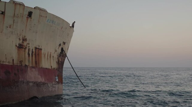 Tourist diving from rusty old shipwreck near the coastline on sunset
