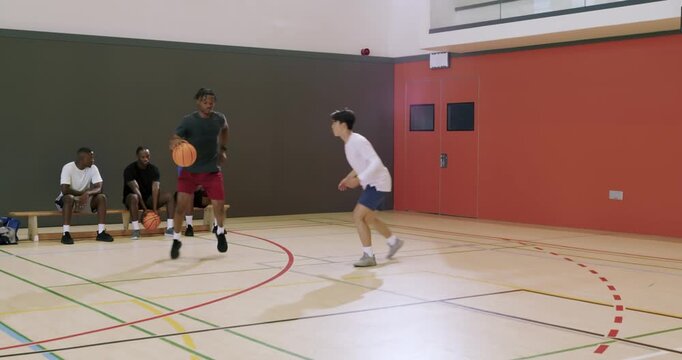 As defender shuffles man dribbling on court, driving baseline, leaping toward hoop