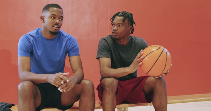 After blue-shirt remark, two men passing basketball while bantering on gym bench