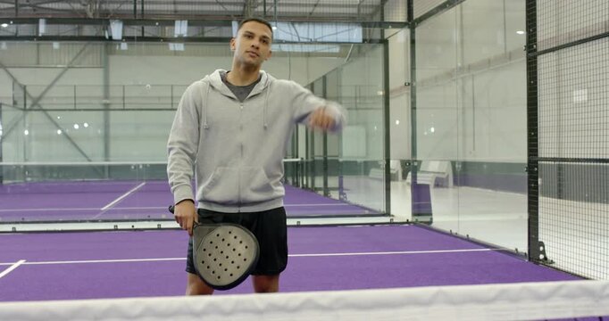 After grabbing racket, man at net on padel court performing ghost swings and strokes, warming up