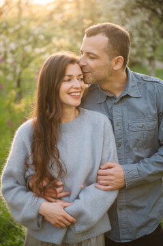 Happy romantic couple portrait. Sincere middle aged husband and wife embrace closely with heads together, smiling warmly in sunny spring or autumn garden at sunset, sharing a tender moment of love.