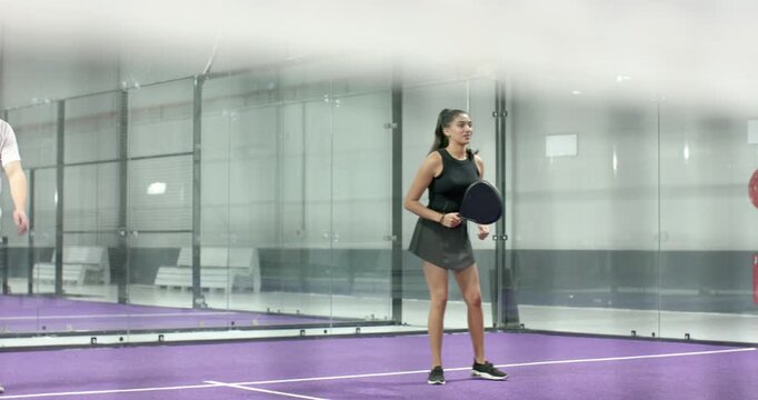 Diverse friends warming up on padel court by rallying ball with paddles, returning shot