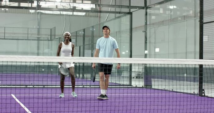 Rally ending diverse sports partners walking to padel net, woman running sideline and fist bump