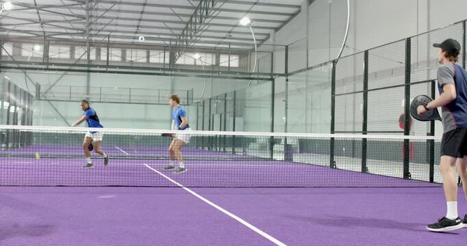 Male players serving yellow ball in glass purple padel court, rallying, shifting into 2v1 drill