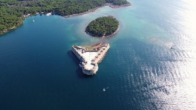 Cinematic straight steady drone video of St. Nicholas Fortress on the Adriatic coast near &Scaron;ibenik, Croatia. The historic stone fortress is surrounded by clear blue sea, turquoise water, pine forest.