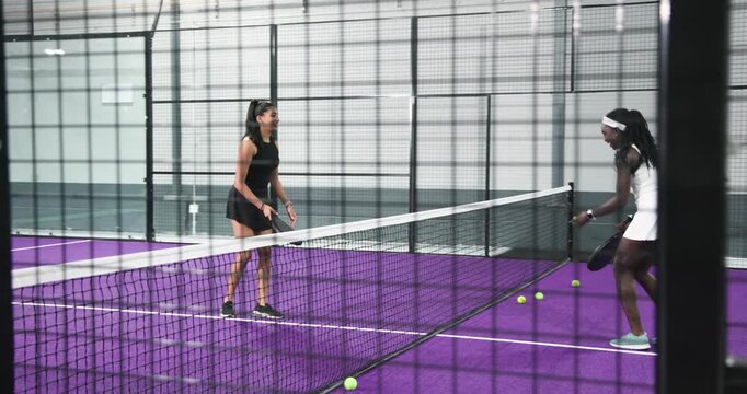 After friendly serve diverse female fiends volleying balls on court collecting and shaking hands