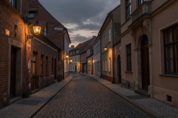 Fototapeta premium A cobblestone alleyway in a historic district comes alive at dusk, with warm street lamps and red brick buildings.