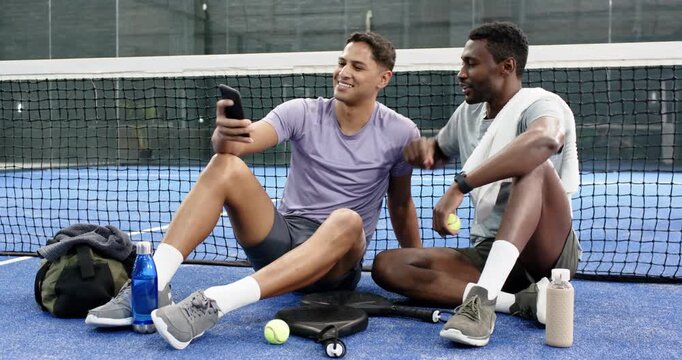 Diverse male friends pulling phone from duffel bag, scrolling photos on tennis court on break