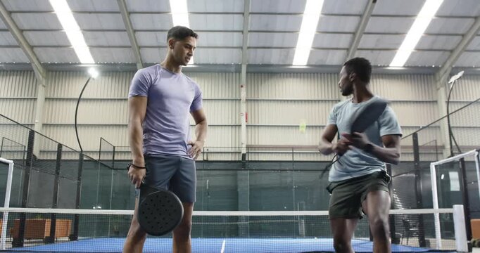 Diverse male friends practicing padel on court, tapping, bouncing balls, volleying