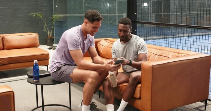 Diverse male friends reacting to smartphone alert, scrolling screen, celebrating on lounge sofa
