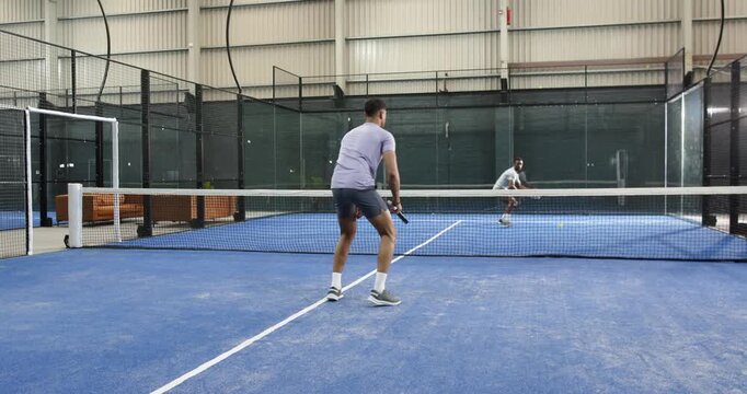 Diverse men starting rally backhanding padel ball over net, hitting forehand on padel court