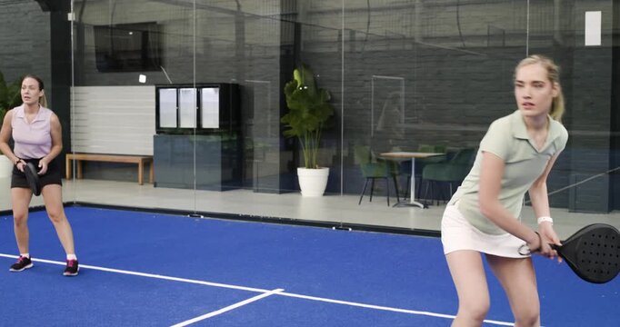 Female sports partners on padel court returning volley after ball serve; celebrating point win