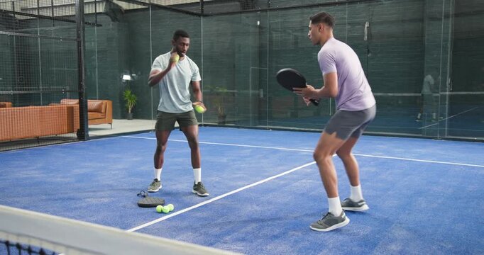 Coach and trainee on blue padel court, feeding balls, returning with racket for technique