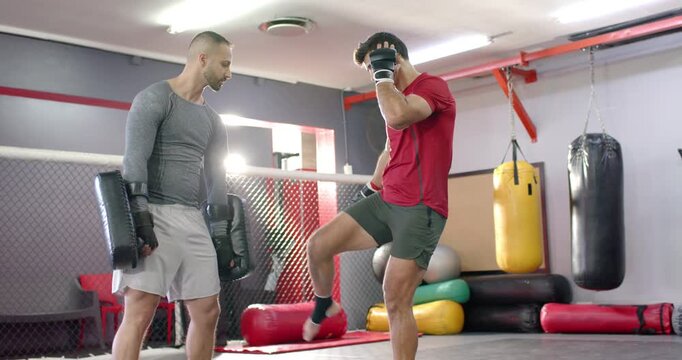 Indian trainer signaling ready with pads as male student kicking, jabbing and landing punch