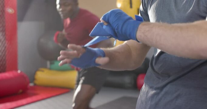 Diverse male boxers wrapping blue wraps, shadowboxing red wraps gearing up in gym, copy space