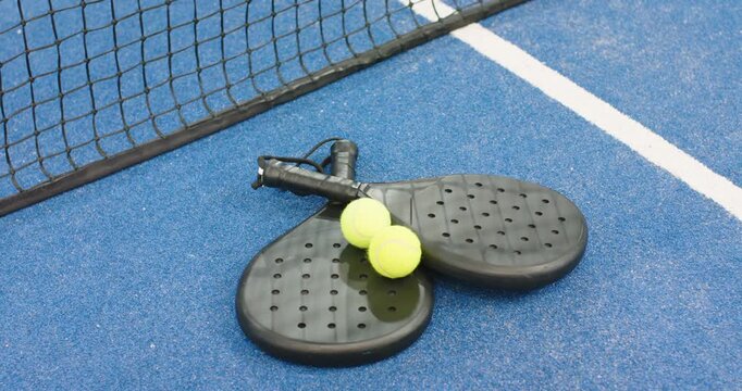 At start padel rackets, balls are resting on blue court at net awaiting match start