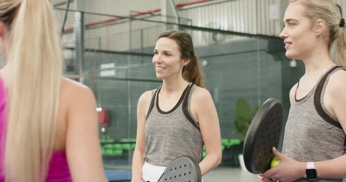 Female group nodding to coach greeting, tapping paddles, practicing forehand swing on court
