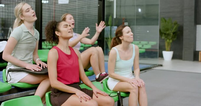 With match intensifying, diverse female friends on bleachers clapping, consoling anxious friend