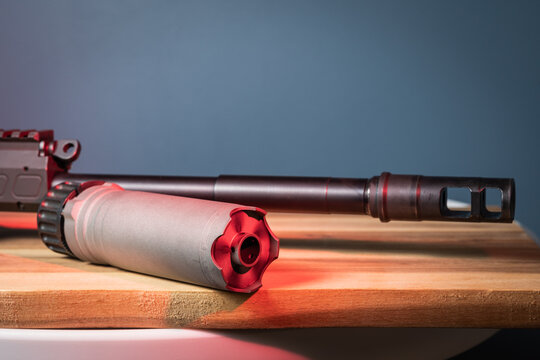 Close-up of a rifle barrel with a muzzle brake and a separate compact suppressor ready for direct attachment on a wooden surface