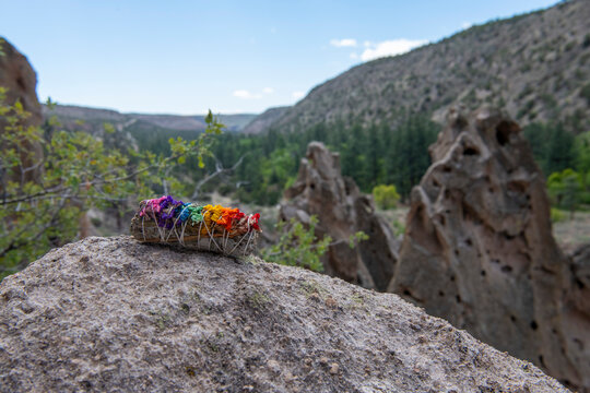 A smudge stick, or bundle of dried herbs, with brightly colored rainbow dried flowers, sits on rock in a rocky outdoor hike, representing growth, movement and pride. 