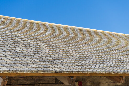 Rustic cedar shake roof texture background with repeating pattern of old wooden tiles. Detailed texture of traditional weathered wooden shingle roof against clear blue sky.