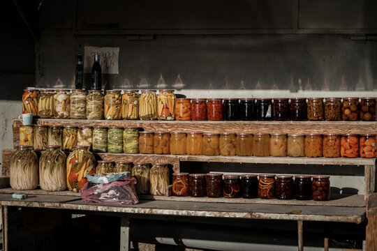 Colorful homemade Armenian pickled vegetables and sweet fruit preserves in glass jars at a rustic roadside stall.