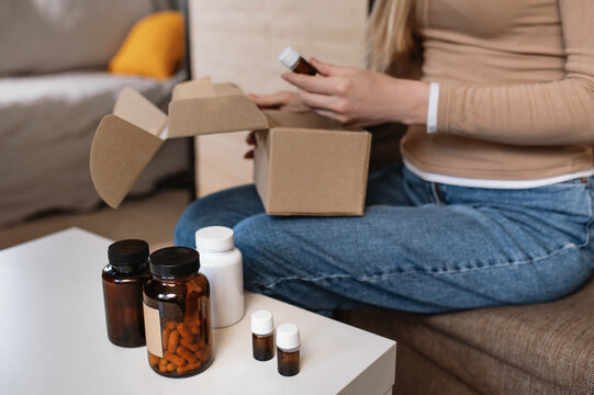 A woman unpacks a package of dietary supplements and vitamins at home. Online shopping and home delivery by courier. Review of a package of vitamins and dietary supplements for vegans.