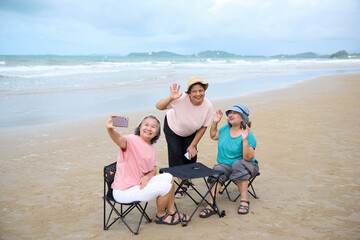 Obraz premium Elderly women happily enjoying a day at the beach, taking selfies and enjoying each other's company. They are sitting on foldable chairs at a small table on the sand.