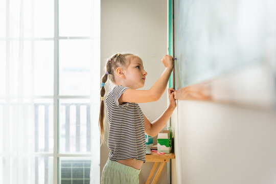 Schoolgirl practicing writing on blackboard during home education, Young girl writing on chalkboard in classroom, education concepts