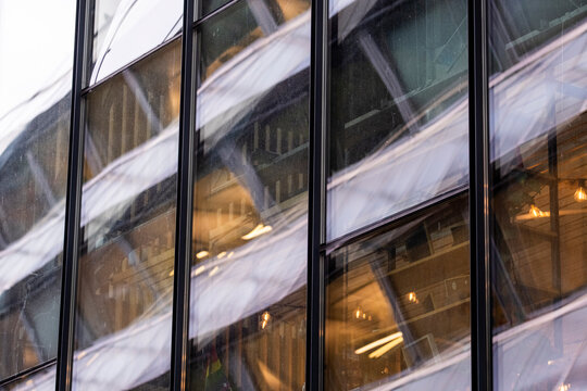 Glass facade reflects blurred building forms and warm interior lights, blending architecture reflection with motion texture across a modern urban exterior