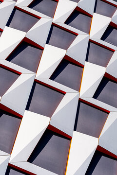 White diagonal facade panels frame dark windows in an abstract architecture pattern, creating sharp geometric texture across a modern urban building exterior