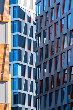 Blue glass facade rises beside dark windows and warm brick detail, giving modern architecture a vertical urban pattern across the building exterior