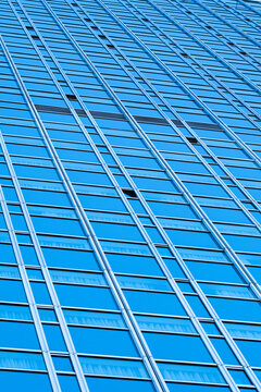 Blue glass grid covers a tall facade with repeated windows, forming an abstract architecture texture across a modern urban building exterior