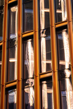 Orange facade columns hold tall windows with glass reflection, turning architecture detail into a vertical urban building exterior of warm lines