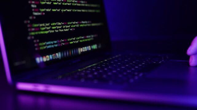 Close up of hand scrolling on a laptop mouse with coding on screen in a dark neon lid room.