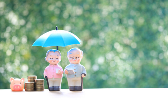 Senior couple figures under blue umbrella with stacks of coins on green background. Concept for retirement insurance, financial protection, elderly wealth management and pension security.