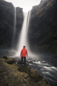 Man in red jacket in front of Kvernufoss waterfall in a gorge, dramatic atmosphere, time exposure, near Sk&oacute;gafoss, Southurland, Iceland
