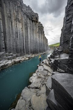 Tourist standing by the river in Stu&eth;lagil Canyon, turquoise blue river between basalt columns, Egilsstadir, Iceland